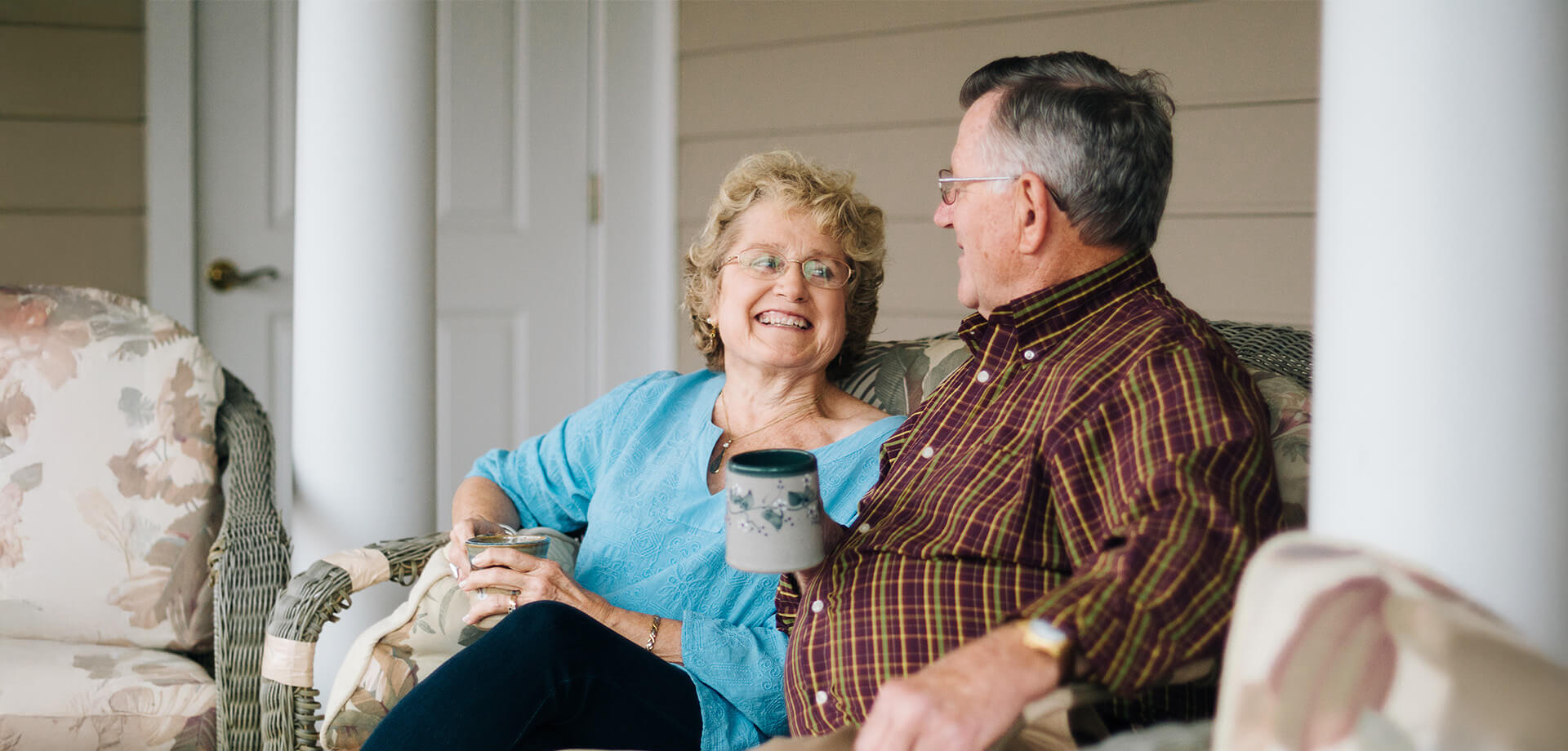 Smiling senior couple enjoying coffee on a unit porch at their living community.