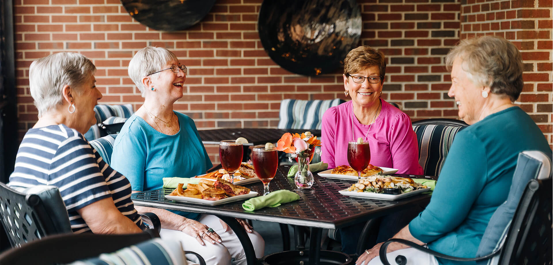 Four elderly women enjoying a meal together at an outdoor dining area.