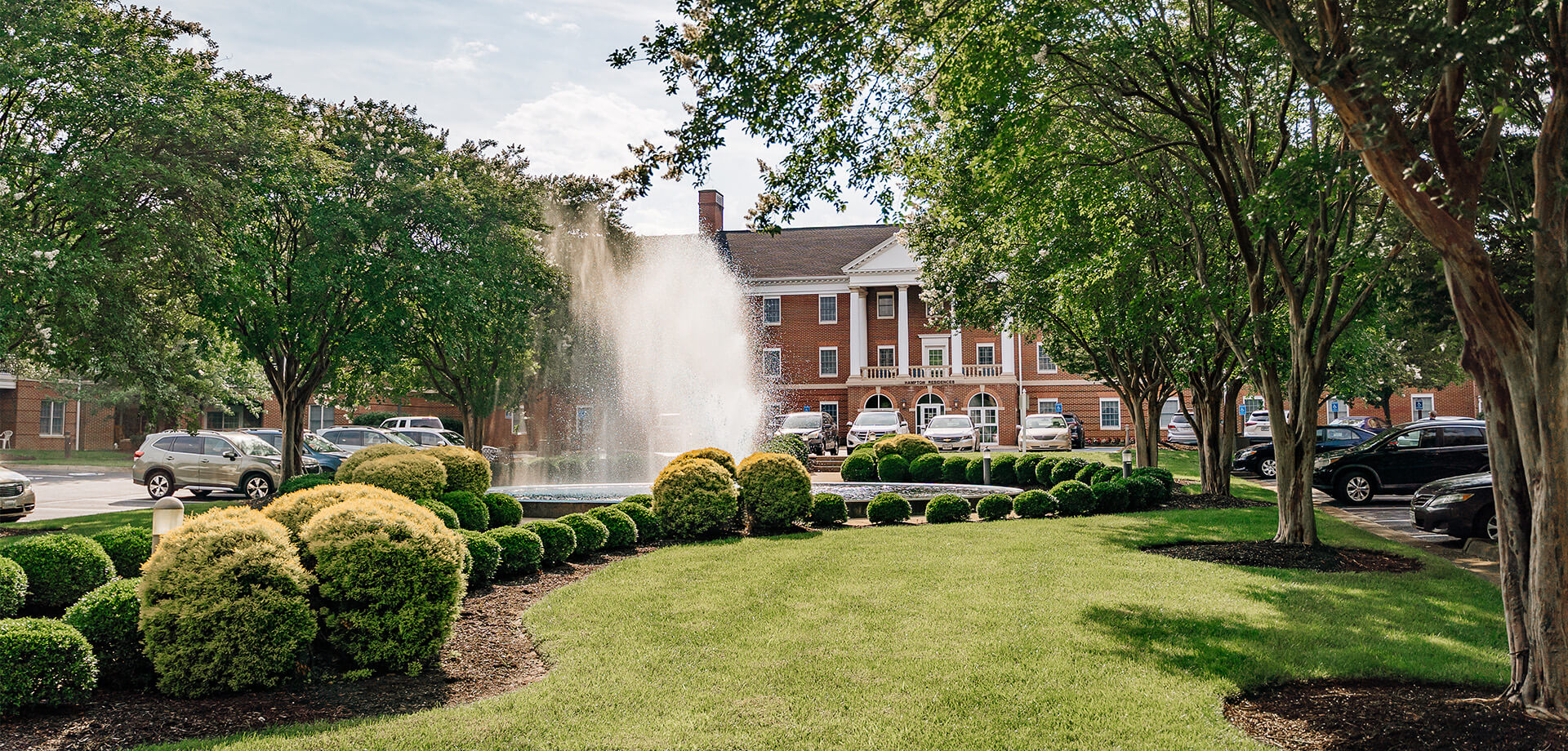 Elegant brick building with a fountain surrounded by lush greenery.