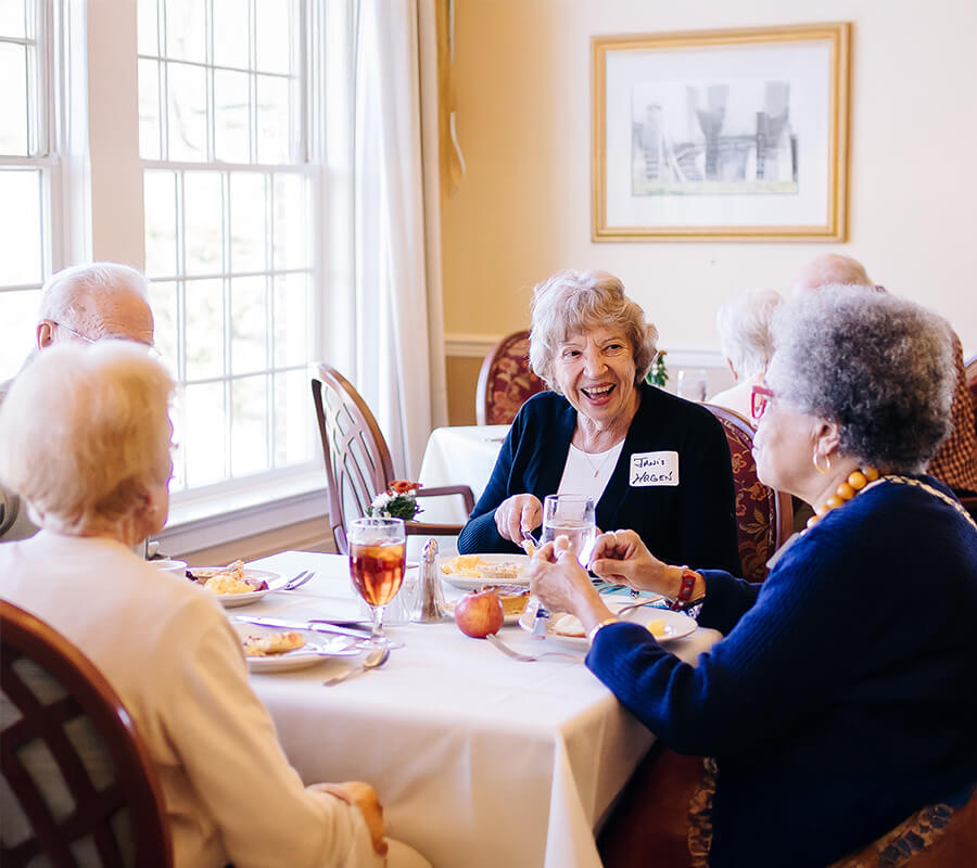Group of seniors dining together, enjoying wine and conversation in a bright room.