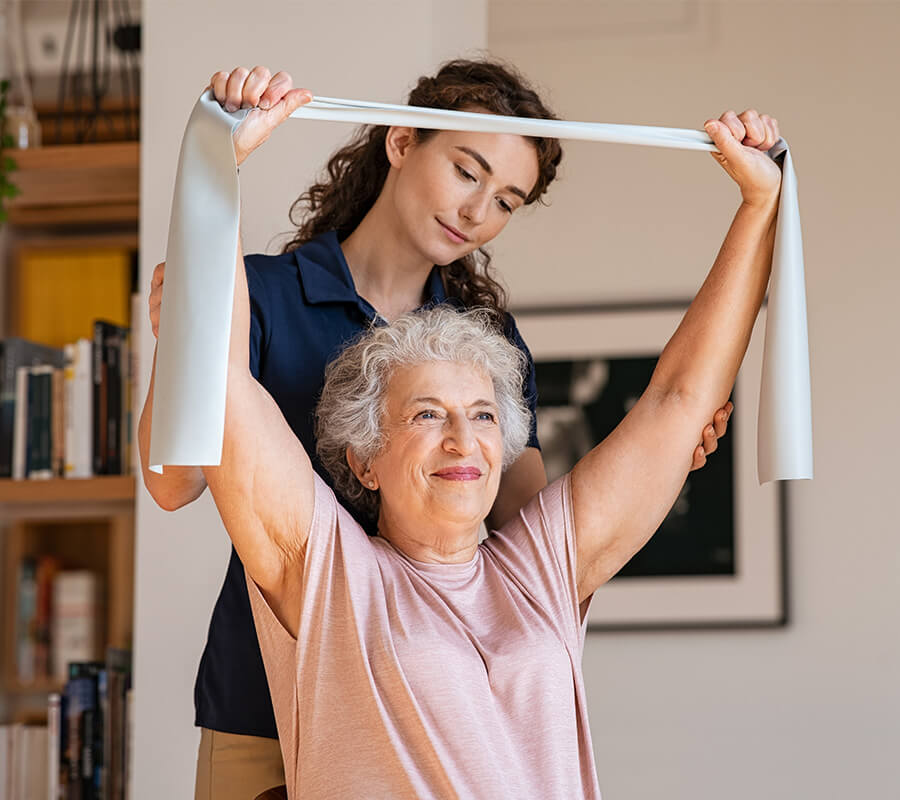 Elderly woman exercising with assistance from a caregiver in a living room.