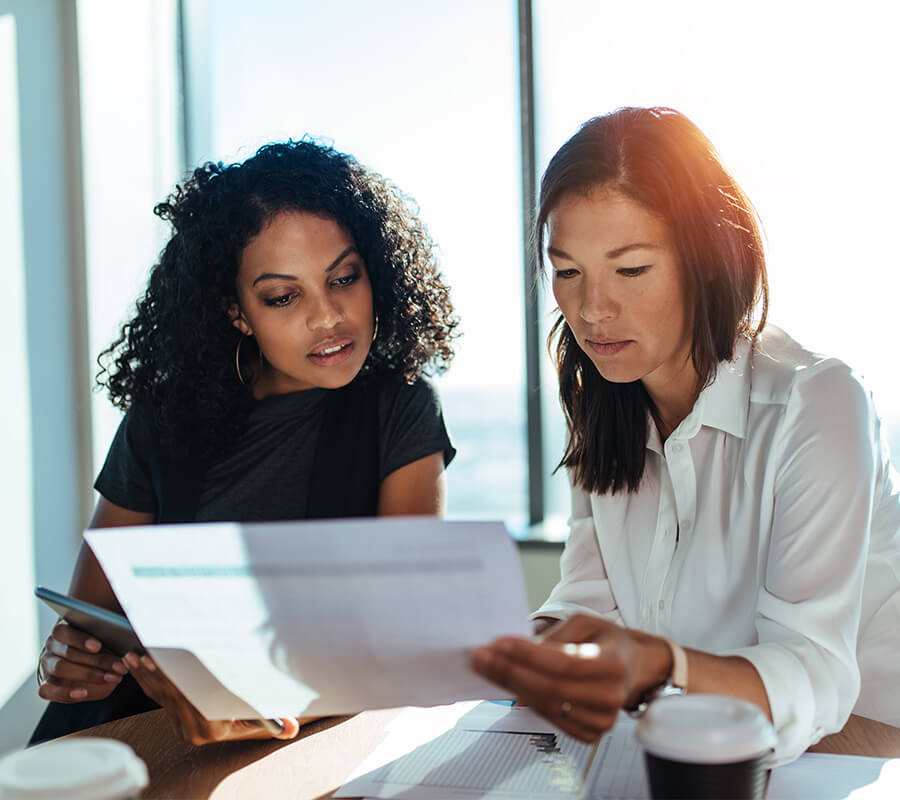 Two women reviewing documents in a sunlit room.