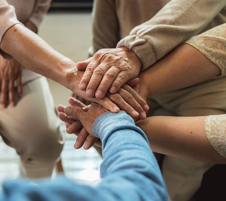 Hands of diverse seniors stacked in a gesture of unity and support.