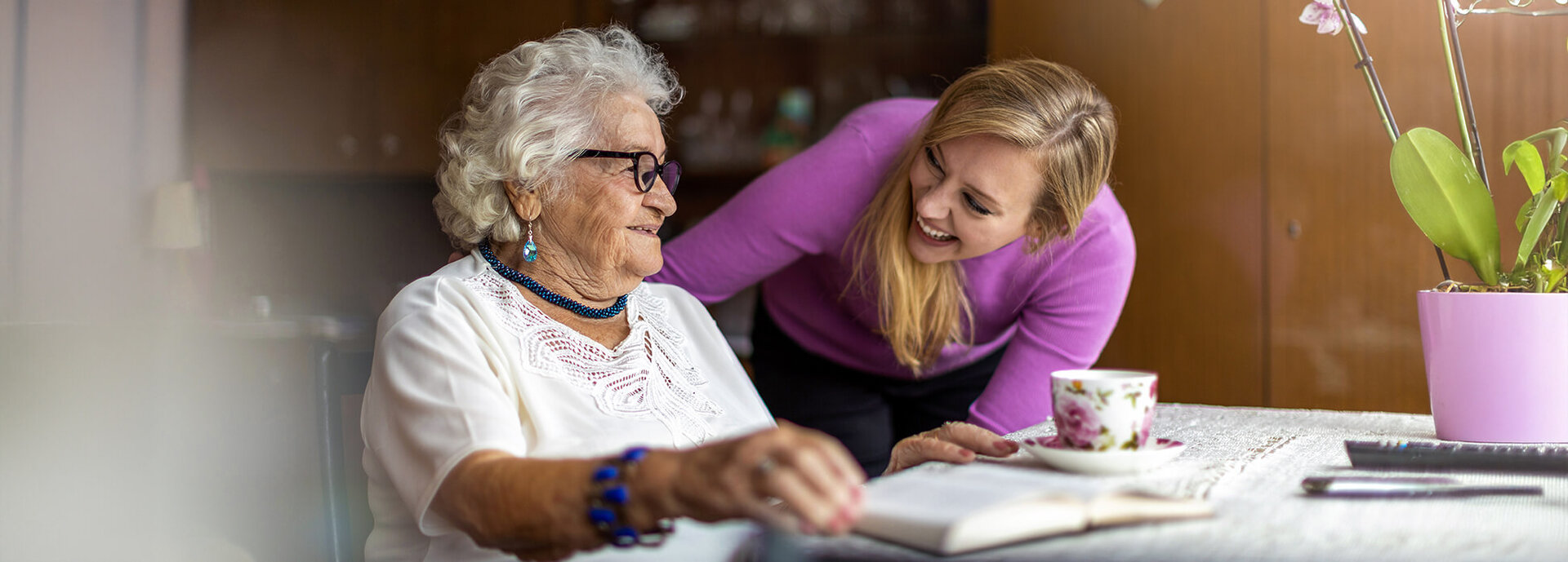 senior woman sitting at desk, talking to a caretaker