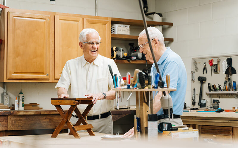 Two elderly men engaging in woodworking in a well-equipped workshop.