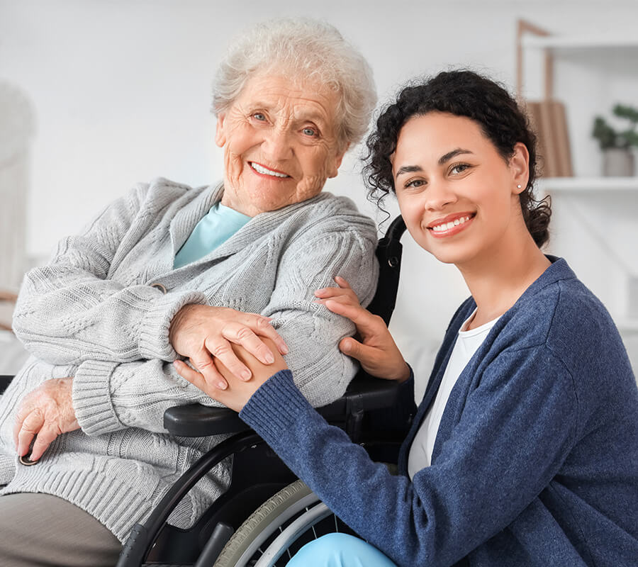 Smiling caregiver with elderly woman in a wheelchair, holding hands warmly.