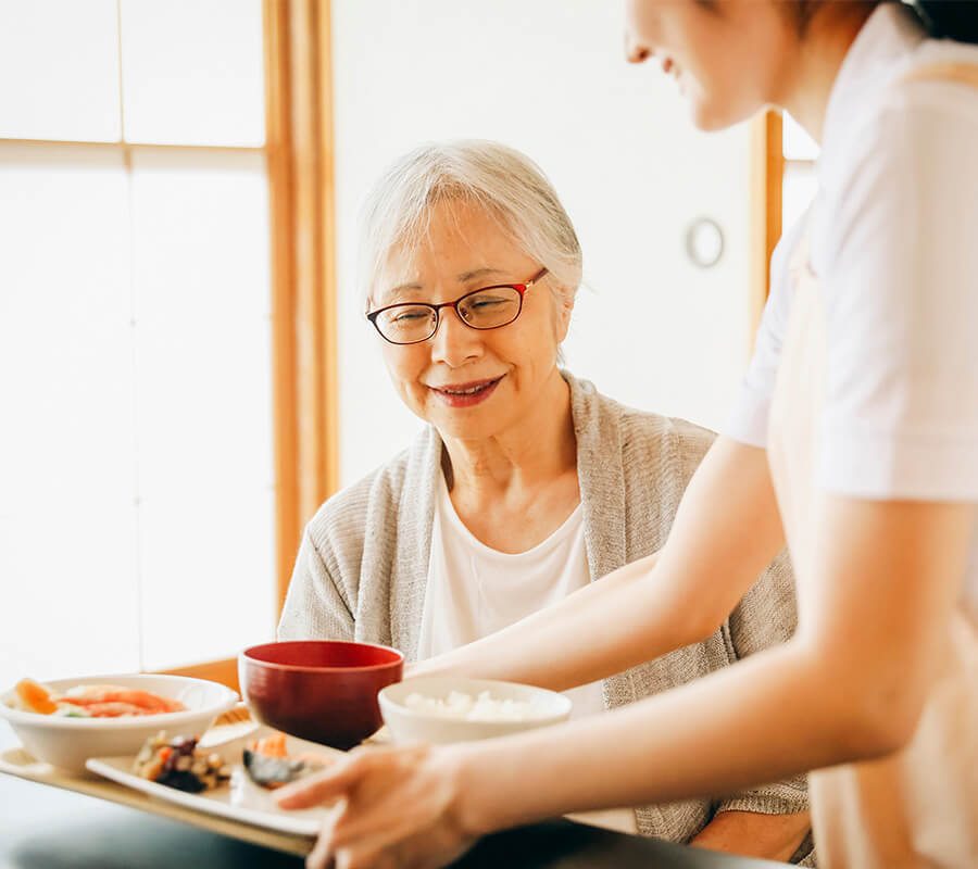 Elderly woman receiving a meal in a well-lit community dining area.