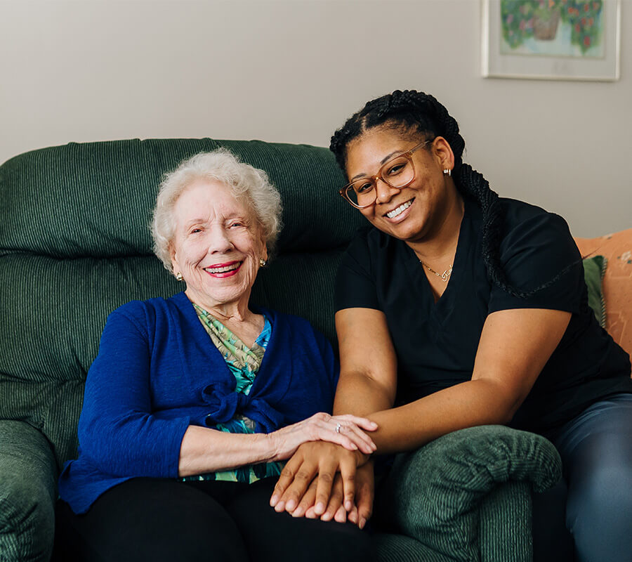 Caregiver and elderly woman smiling together in a living room setting.