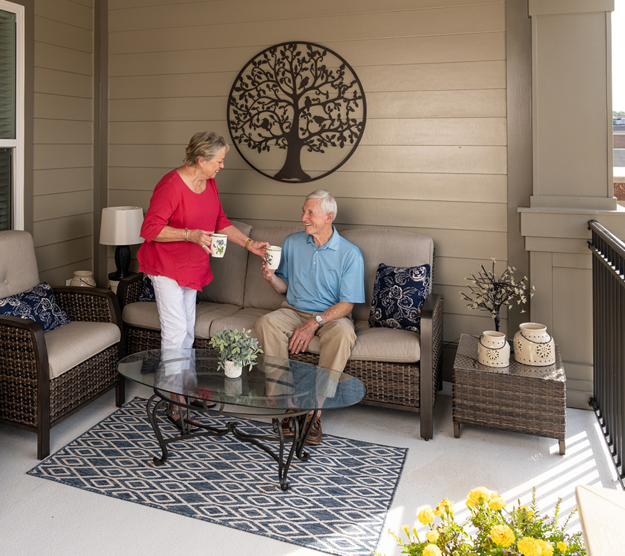 Relaxing Patio Moment Couple enjoying coffee on patio with wicker furniture and decorative wall art.