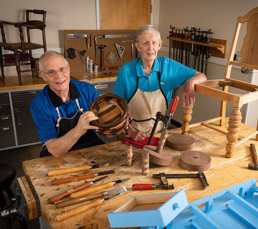 Two older adults engaging in woodworking at a workshop in a community setting.