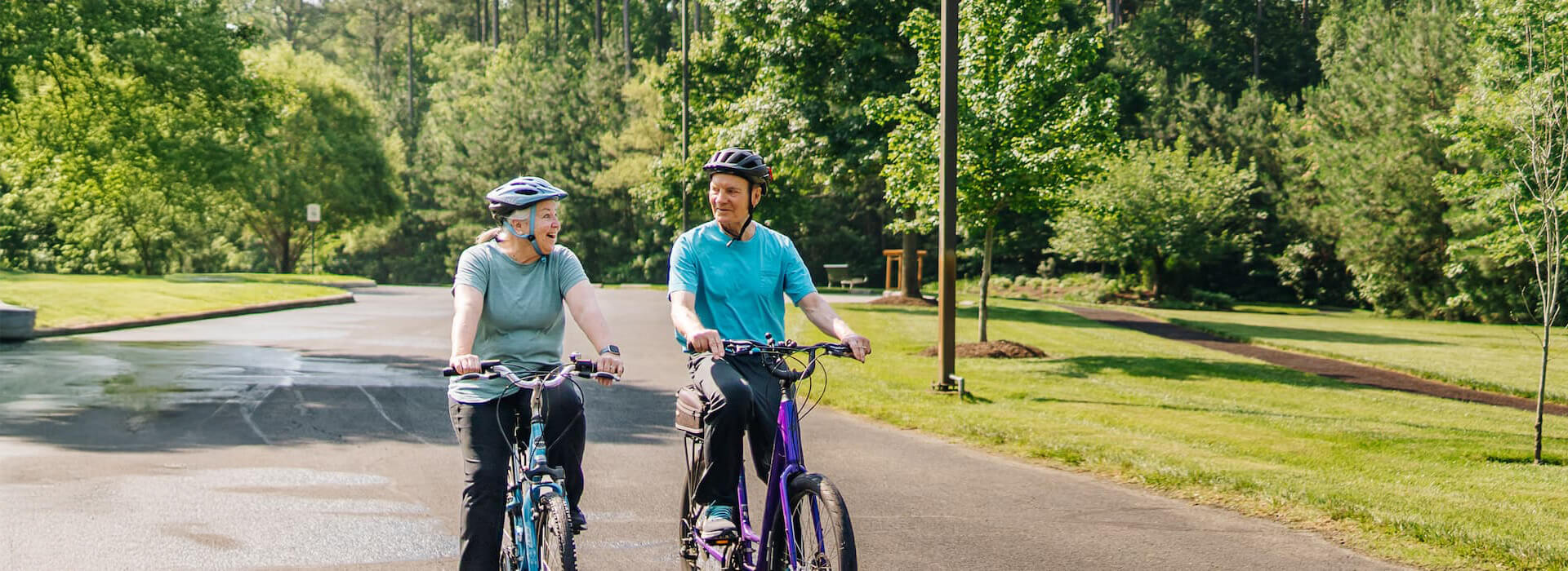 Two seniors ride bikes outdoors on a sunny street