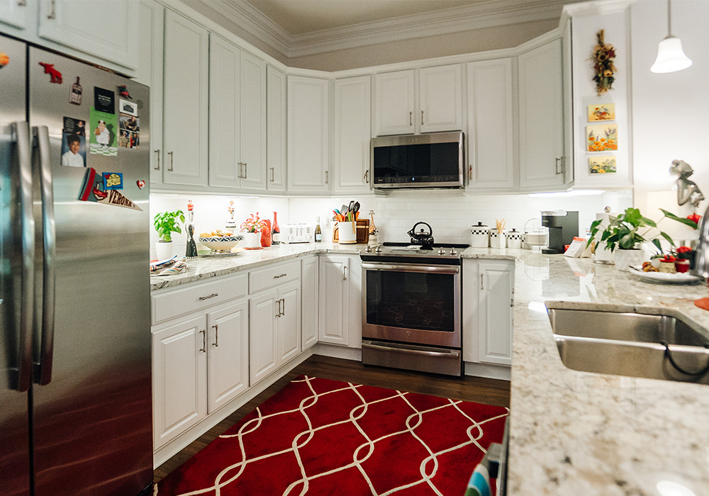 Modern kitchen with white cabinets, stainless steel appliances, and a red rug.