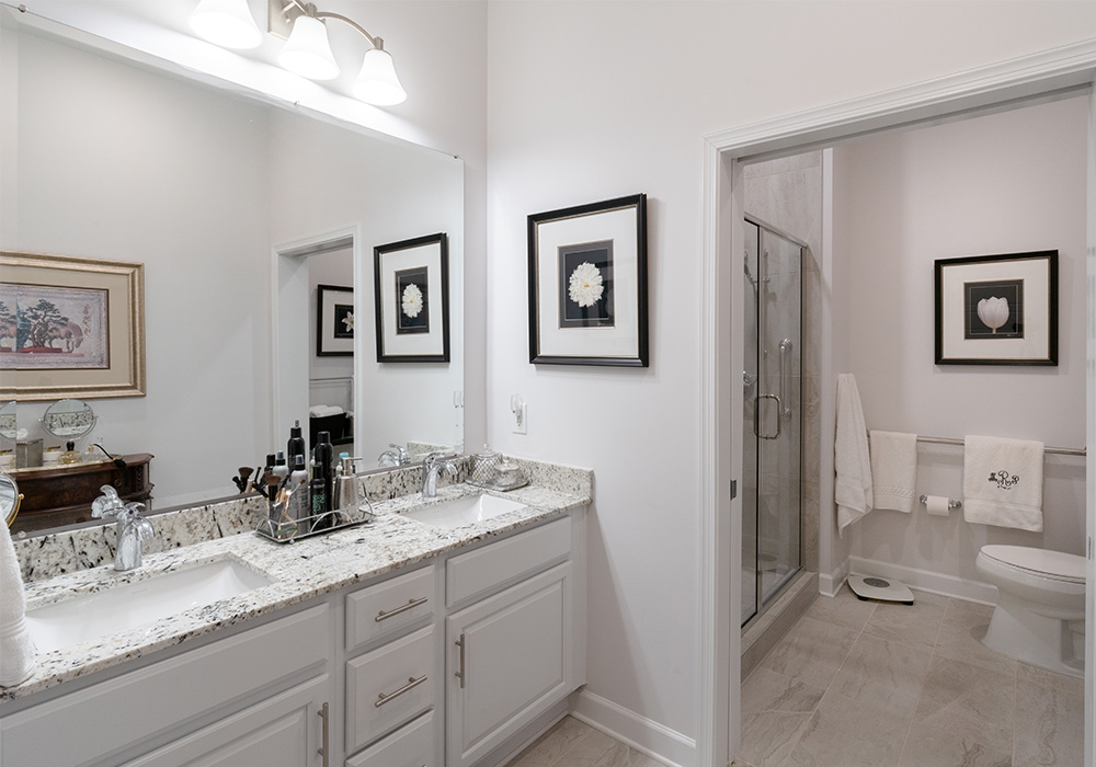 Spacious bathroom with double sink vanity and glass shower in a living unit.