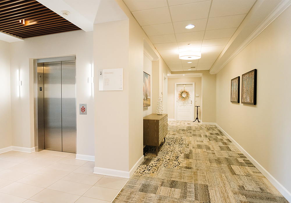 Bright corridor in a senior living community with an elevator and art on the walls.