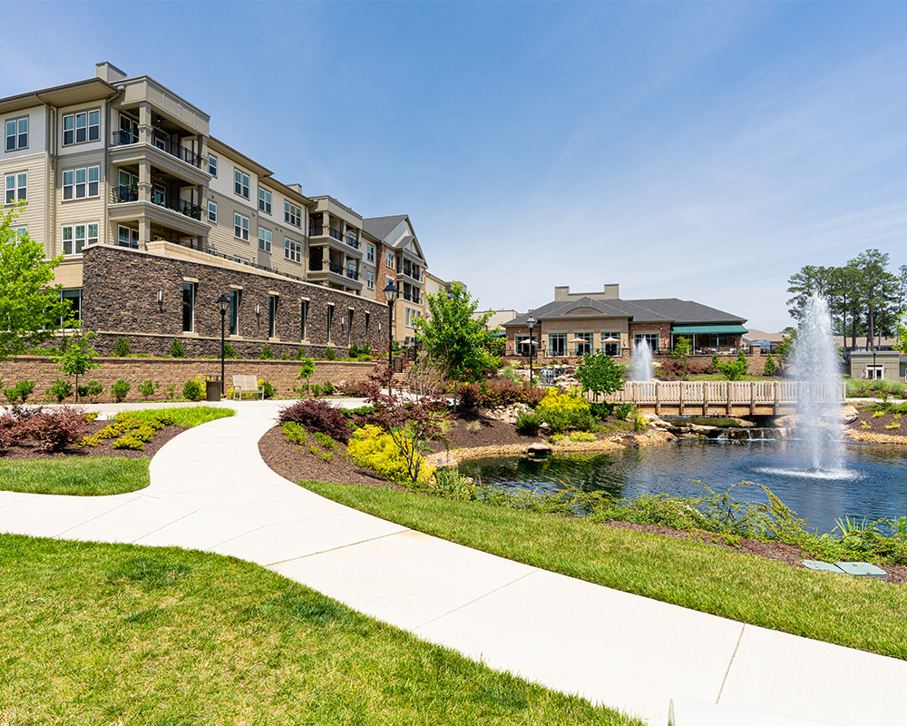 Scenic view of a senior living community with a pond and fountain.