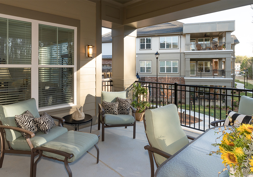 Comfortable patio overlooks garden and three-story residential building.
