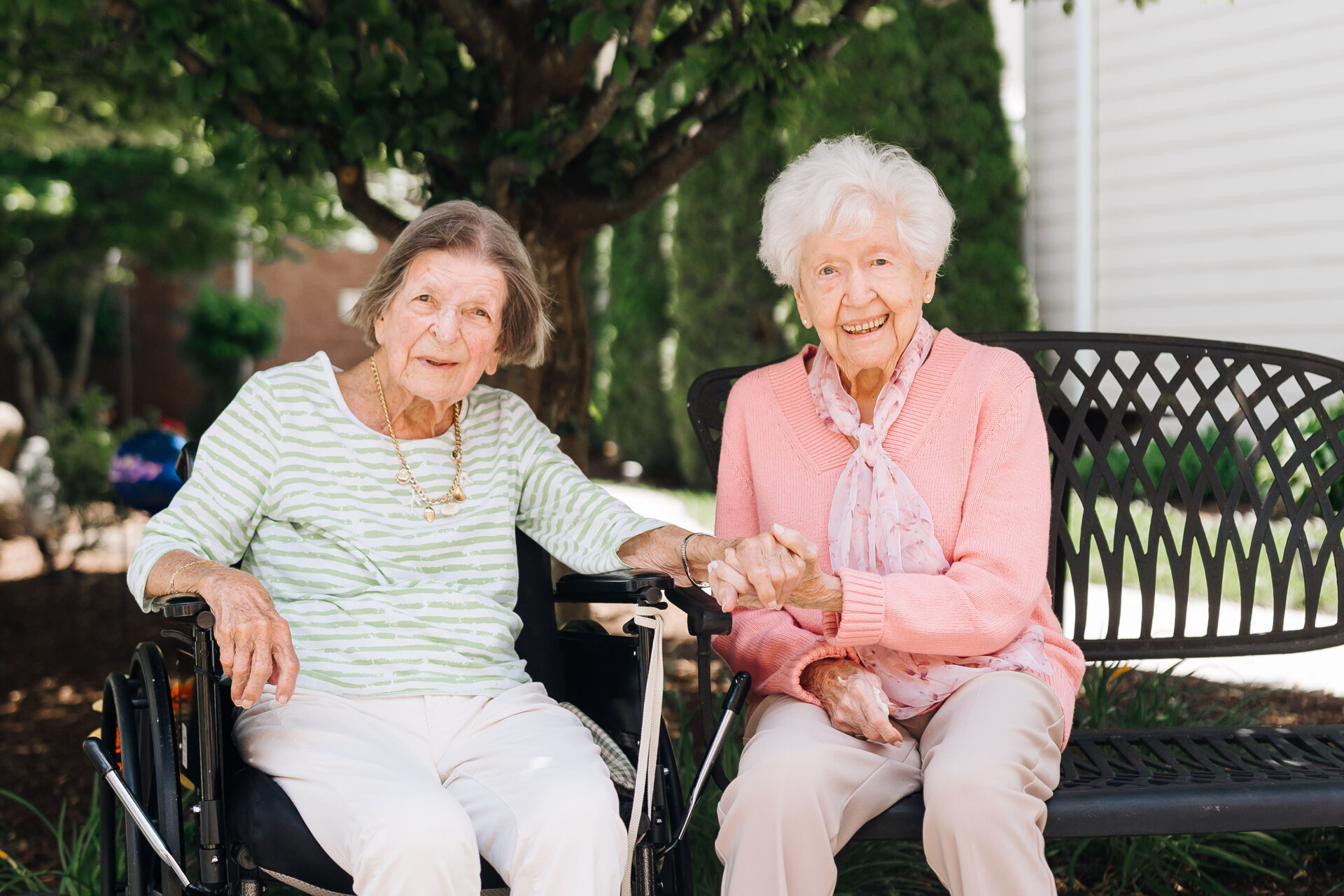 Happy senior women sitting on a bench holding hands