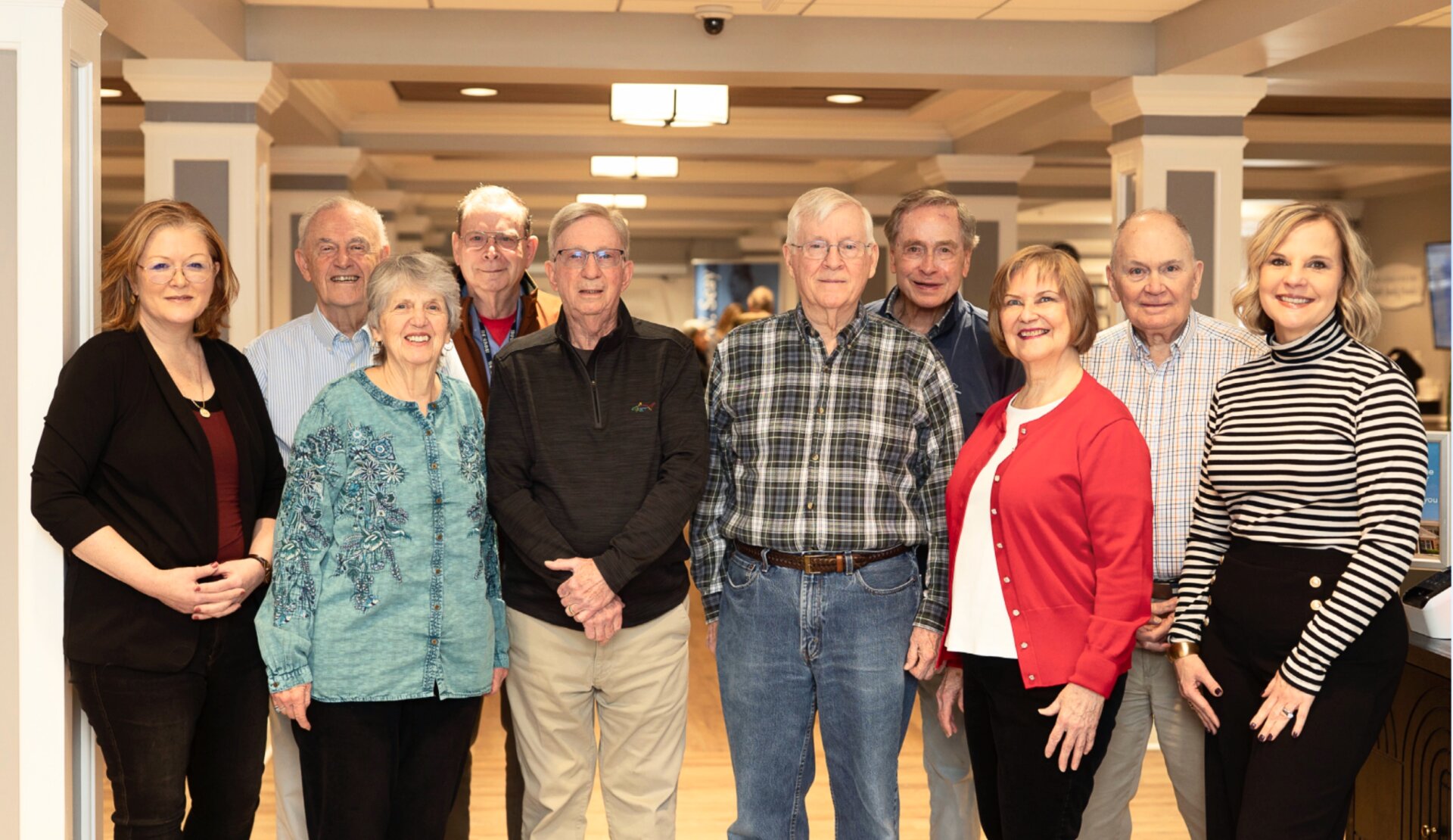 A diverse group of twelve individuals smiles together in a welcoming indoor setting, promoting community and service.