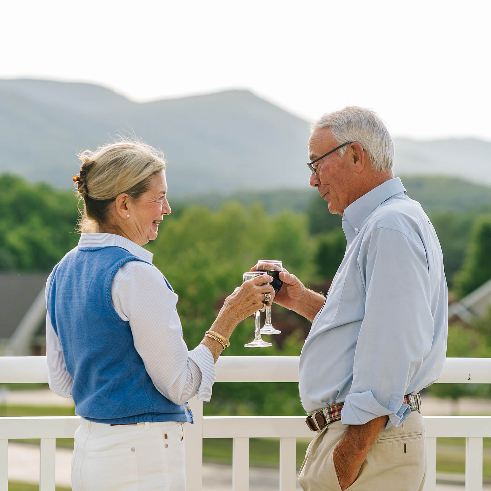 Two seniors enjoying wine on balcony with mountain background.