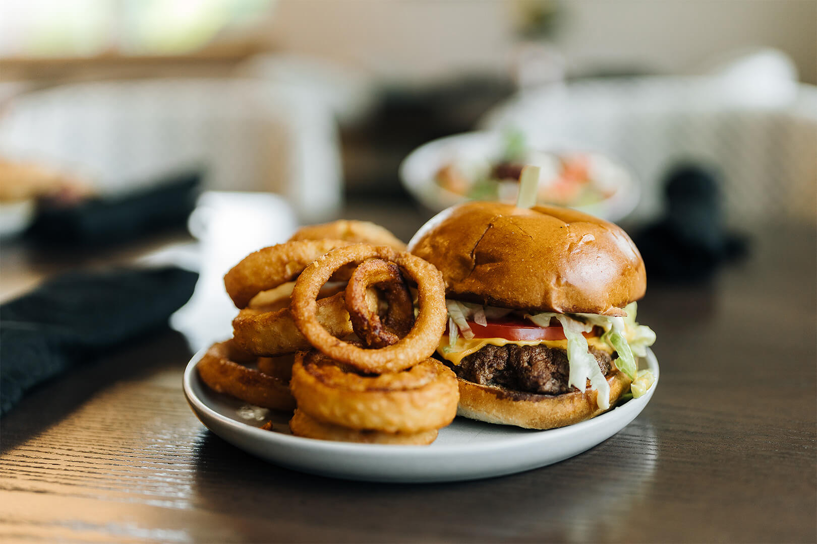 Cheeseburger with onion rings on a white plate on a wooden table.