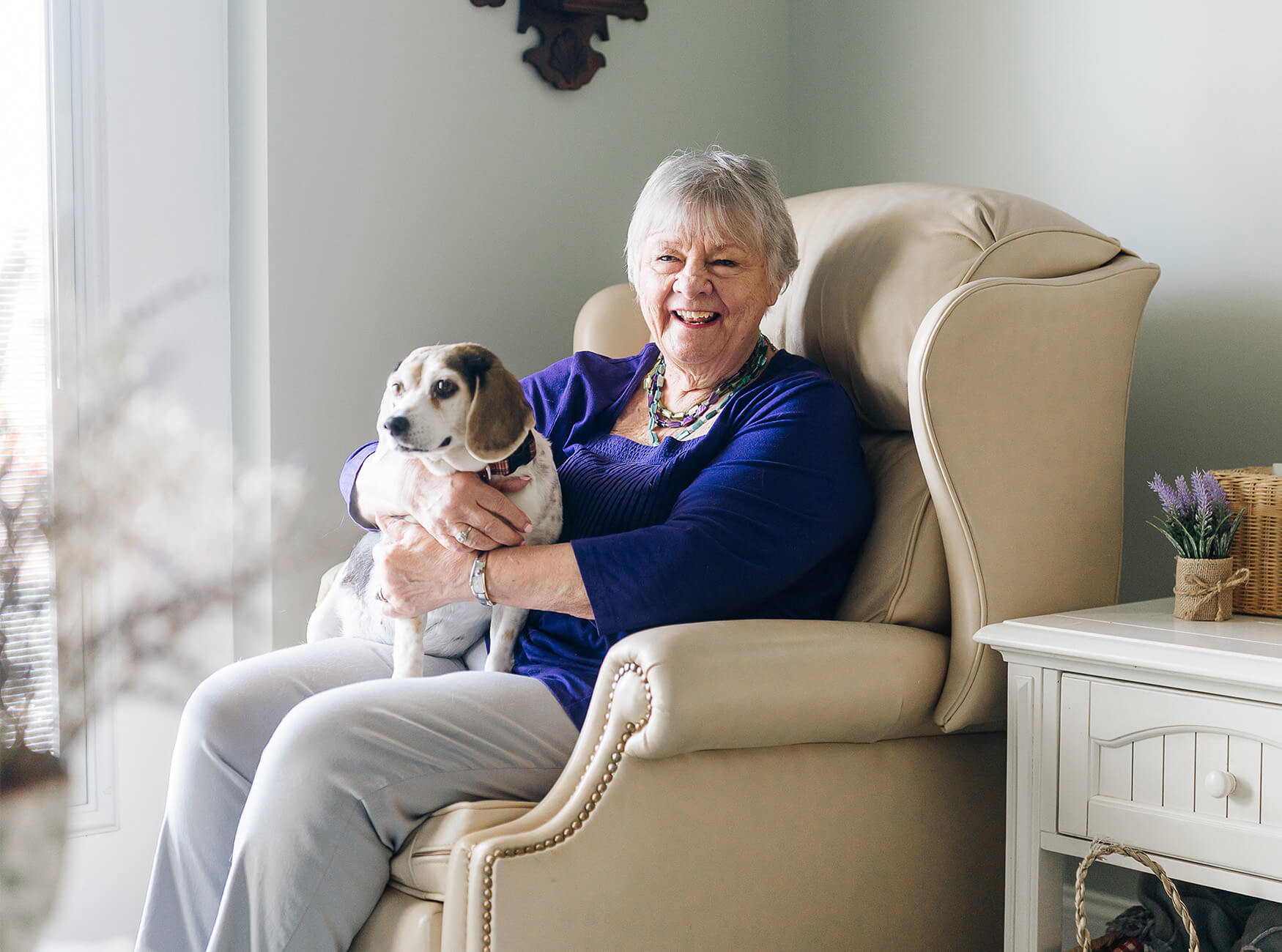 Elderly woman smiling while holding a small dog in a cozy living space.