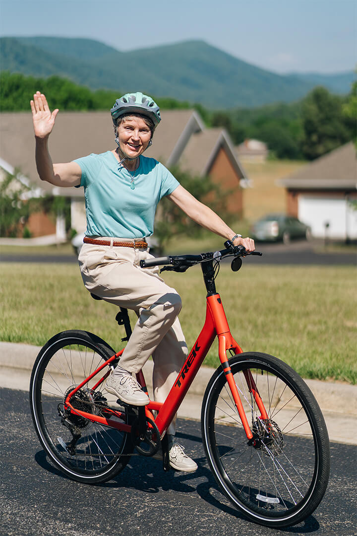 Elderly woman cycling and waving in a peaceful residential area.