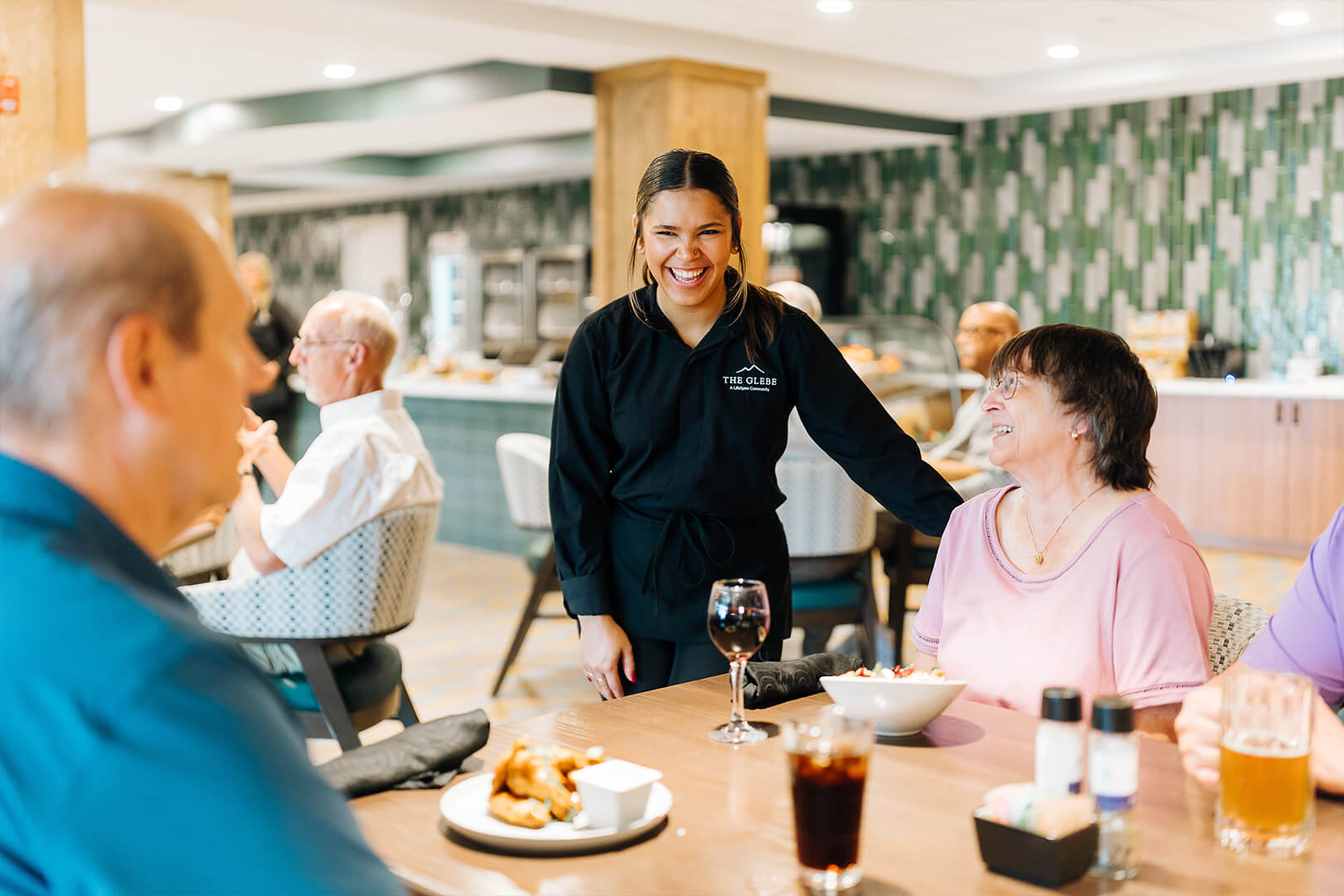 Smiling staff member interacting with residents in a dining area of a senior living community.