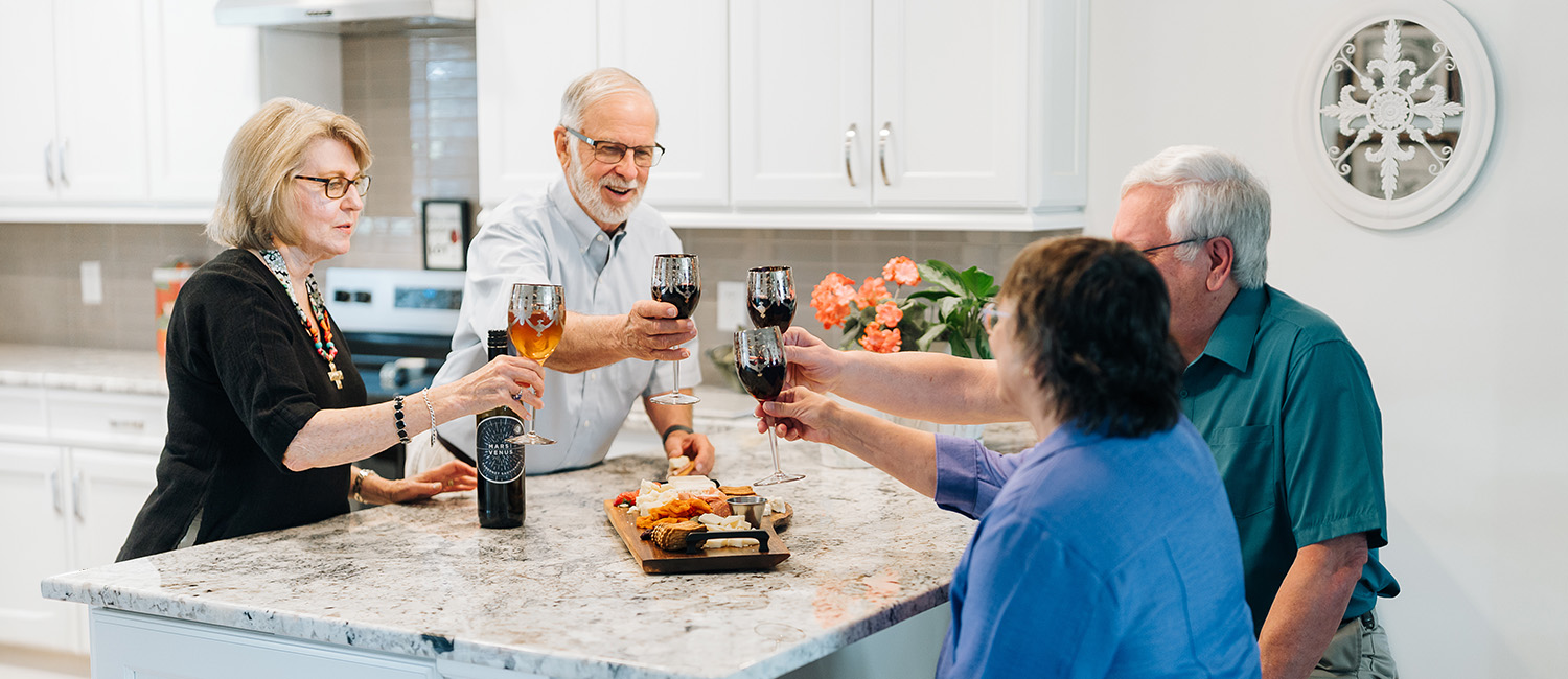Senior friends toasting wine glasses around kitchen table