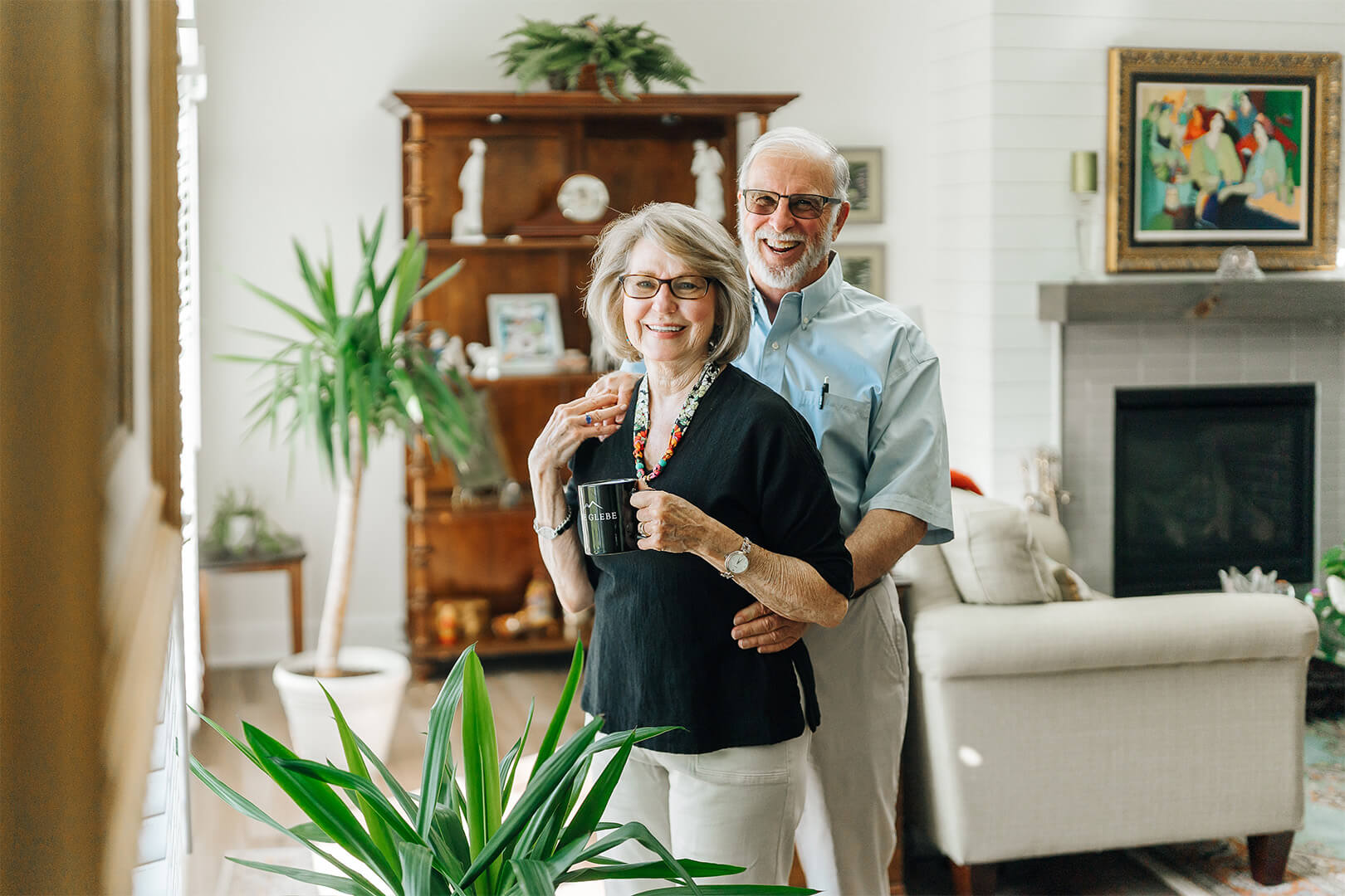 A smiling older couple in a cozy living room setting with plants and decor.