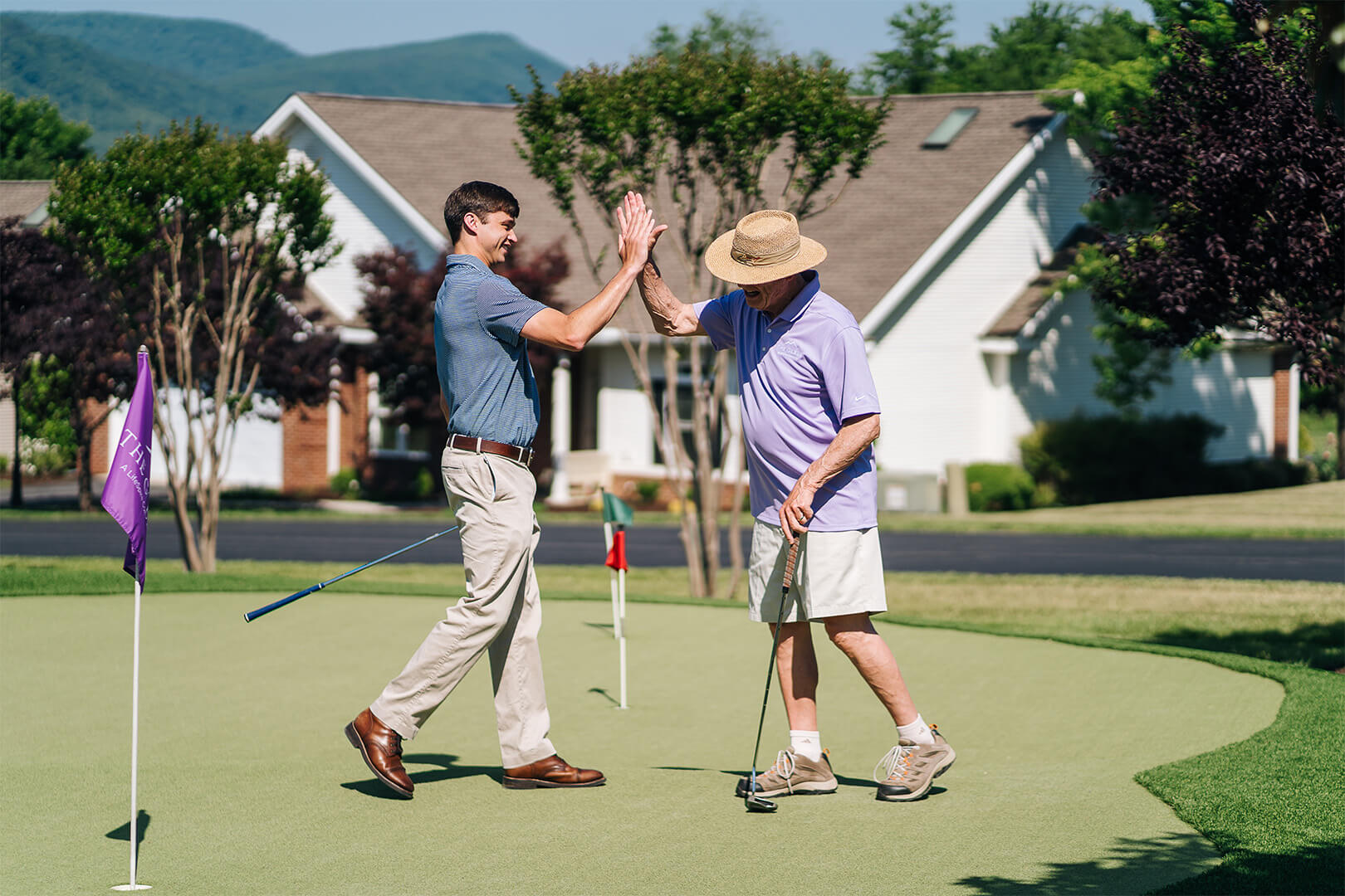 Two men high-fiving on a putting green with residential units in the background.