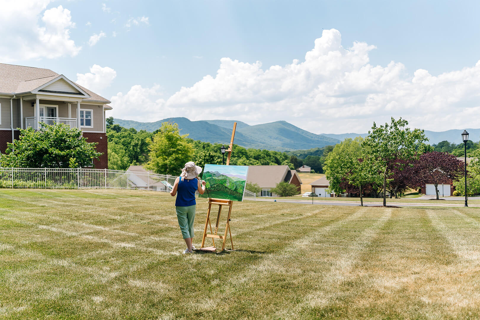 Person painting outdoors in a scenic community with mountains in the background.