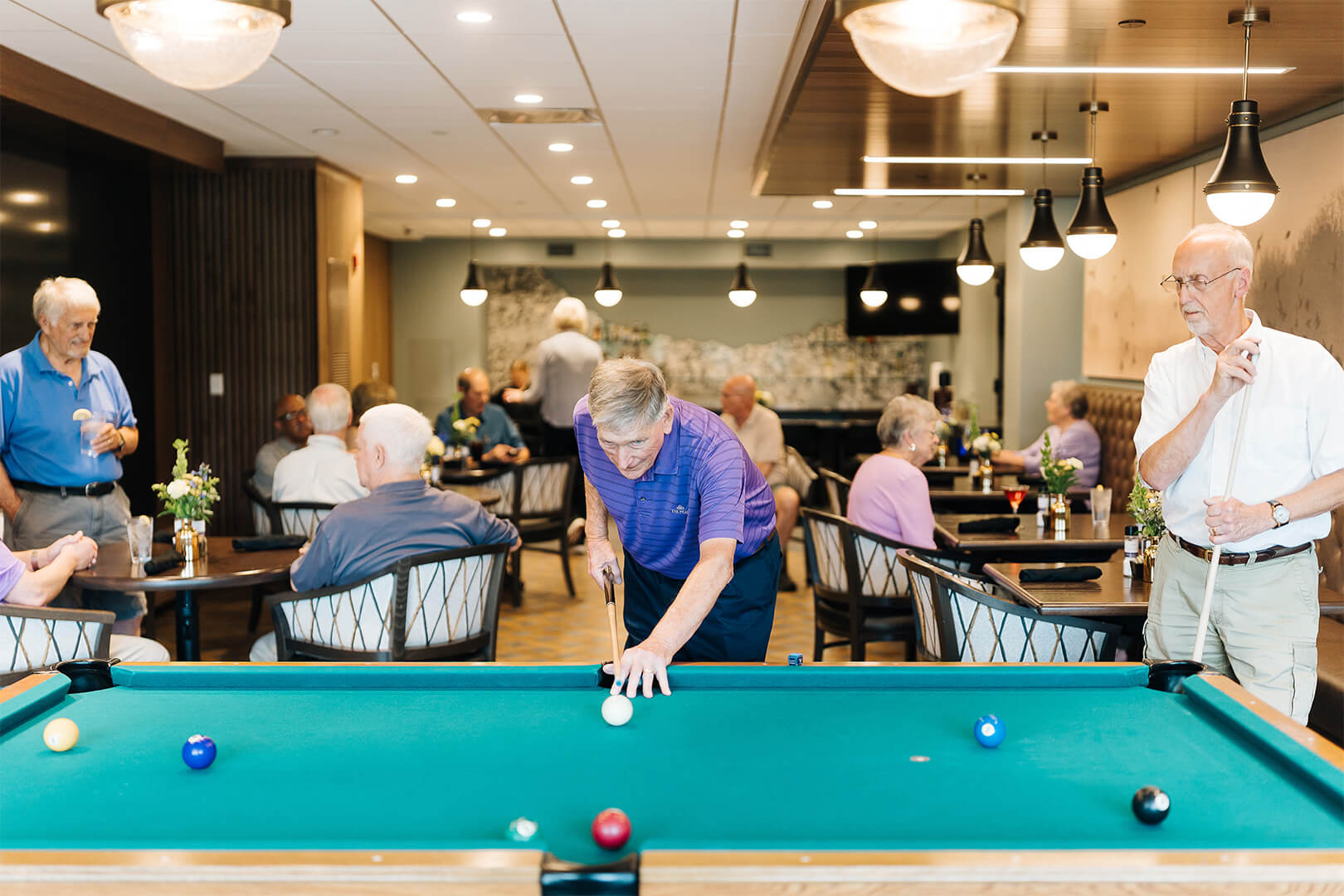 Group of seniors playing pool and relaxing in a community recreation room.