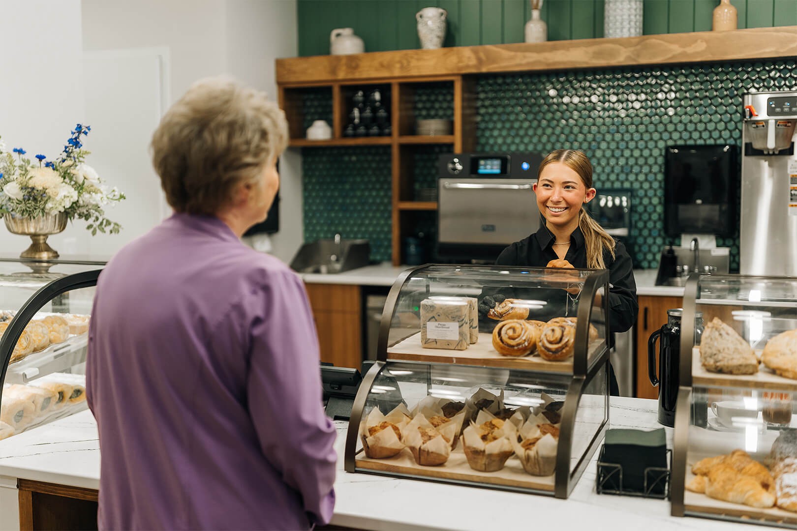 Smiling staff serves resident pastries at senior community cafe.
