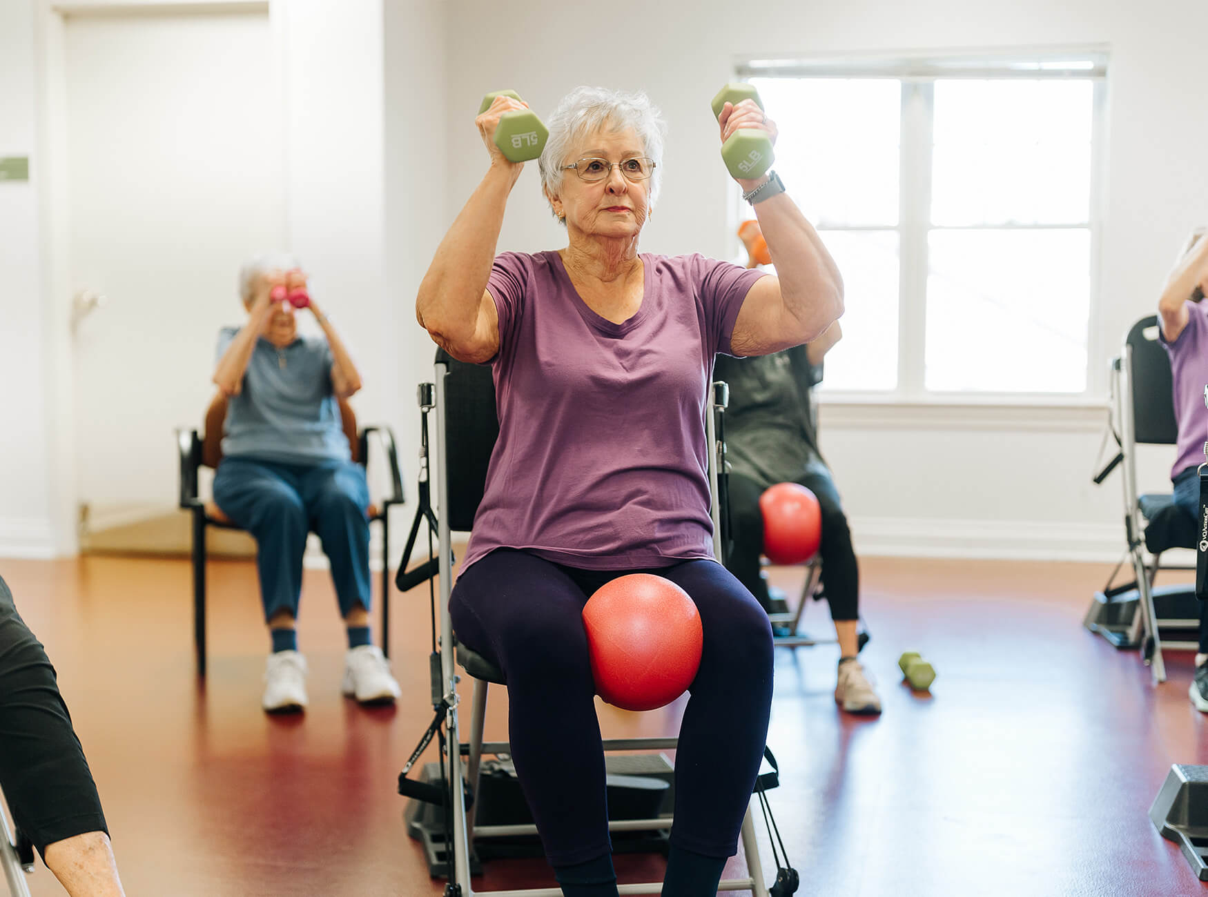 A senior woman exercises with dumbbells in a group fitness at a living community.