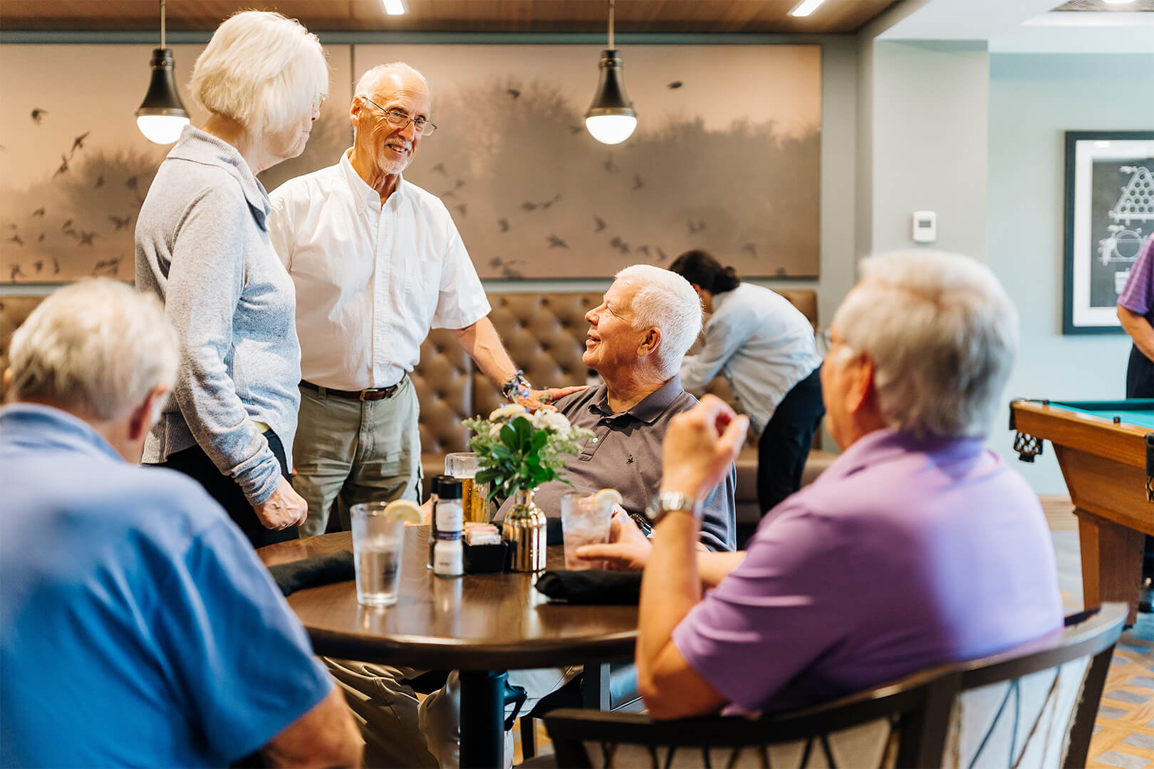 Senior residents enjoy socializing and dining together in a community lounge area.