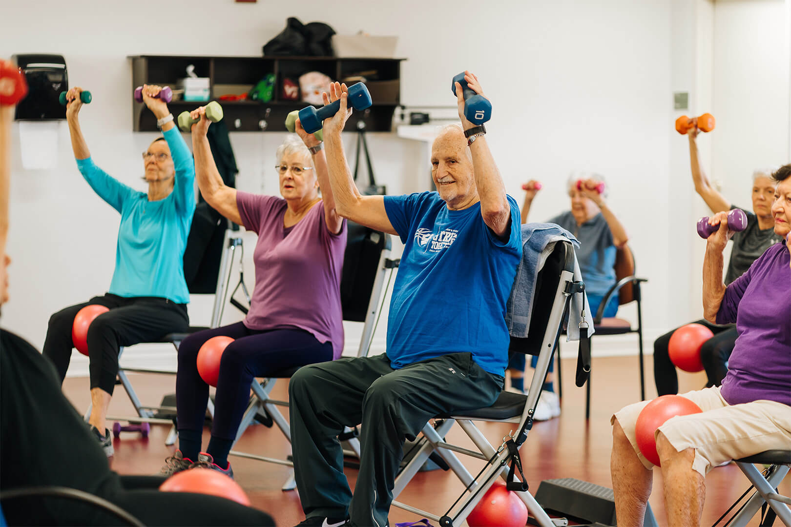 Seniors engaging in chair exercises with dumbbells in a community room.