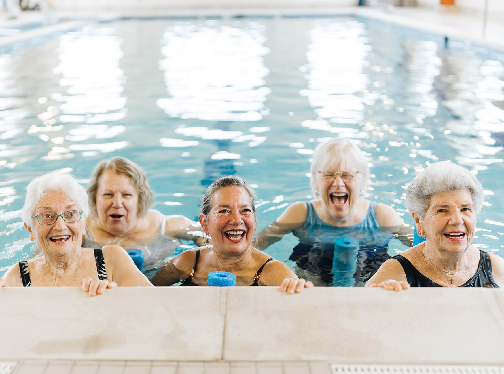Five smiling seniors enjoying a swim in the community pool.
