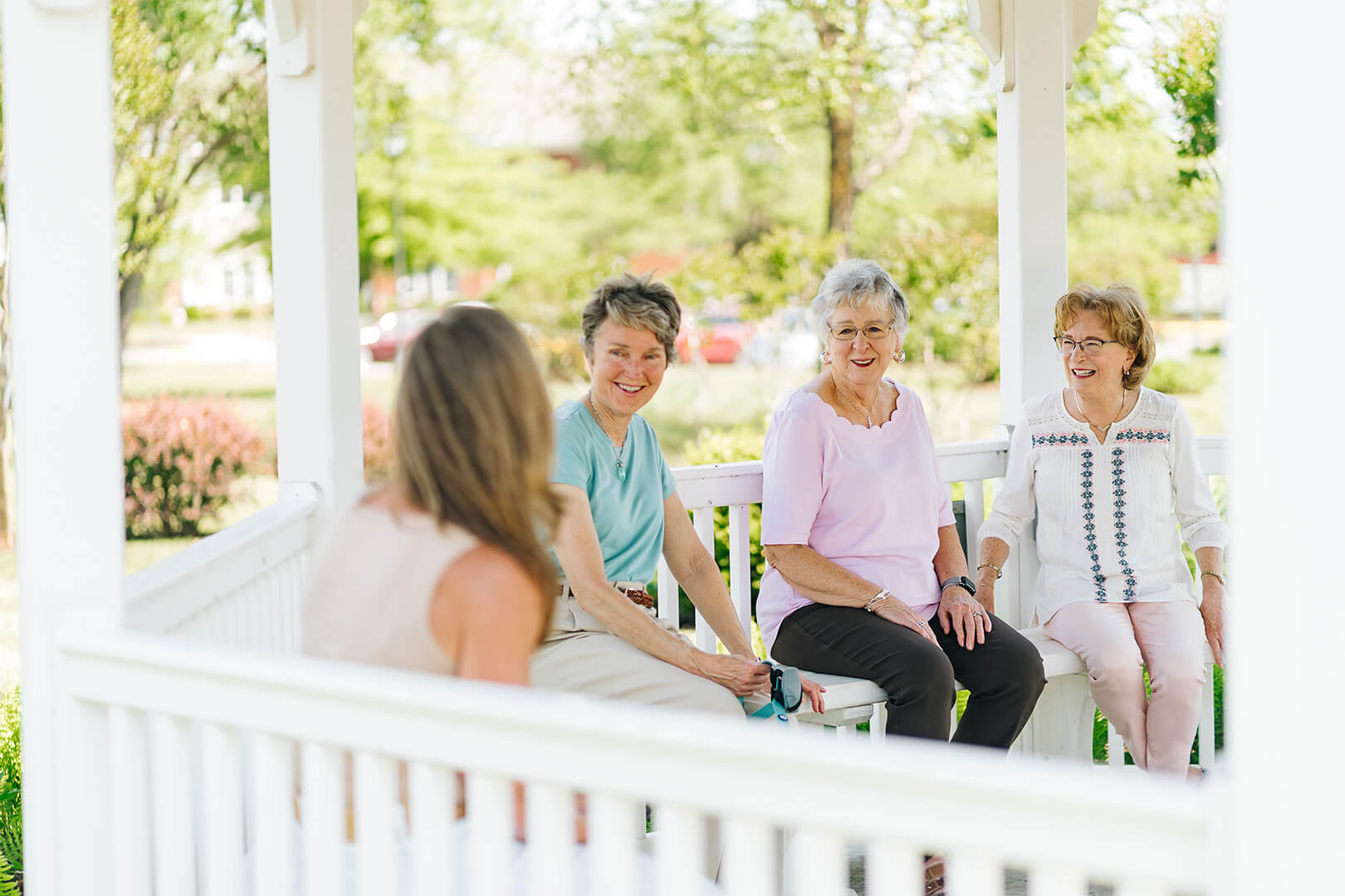 Four women sitting on a porch, smiling and enjoying a sunny day together.