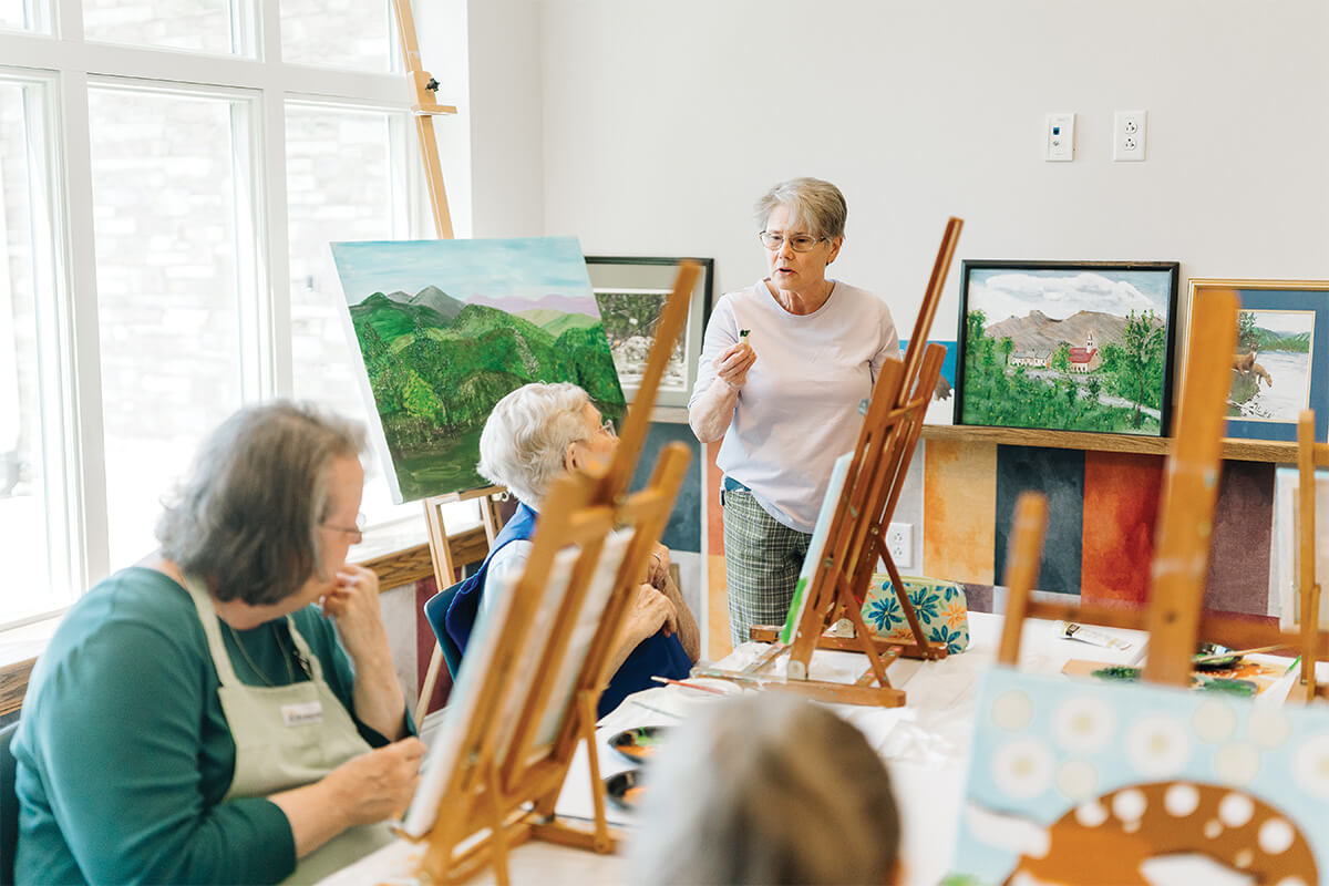 Seniors painting in a with a variety of landscape art displayed around them.