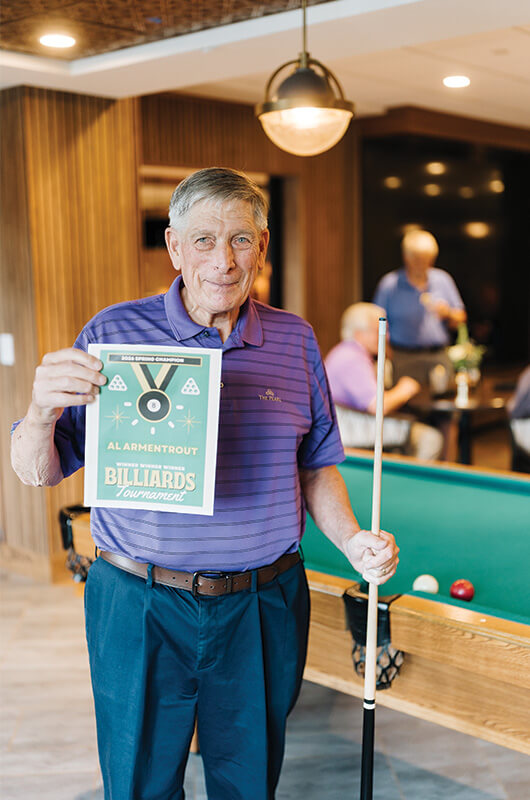 Man holding billiards tournament sign next to a pool table in a recreation room.