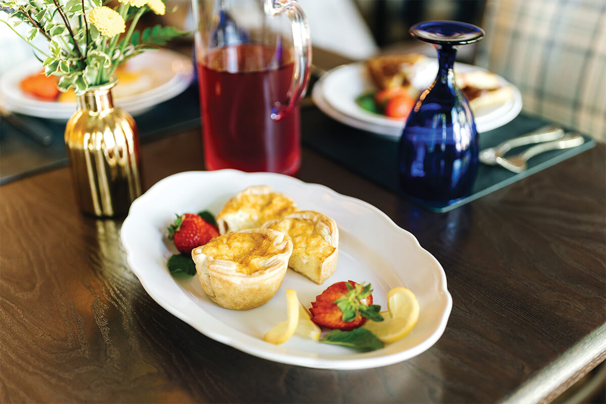 Elegant table setting with quiche, strawberries, and vase of flowers.