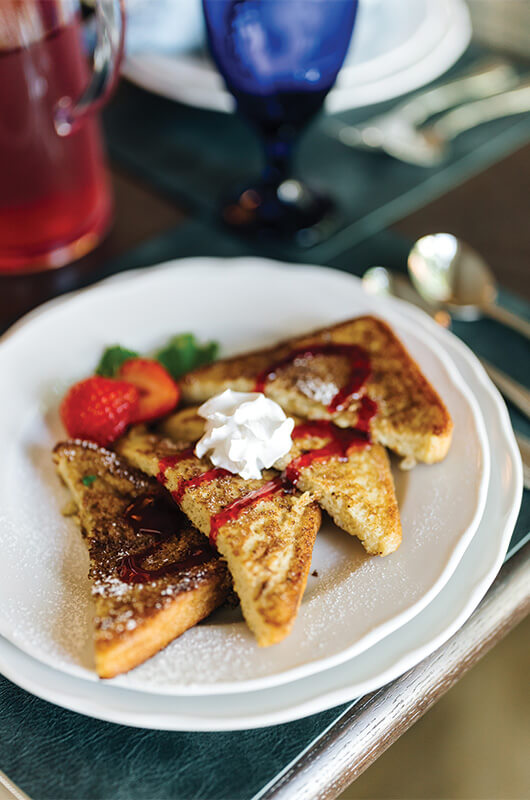 French toast topped with whipped cream and strawberries on a white plate.