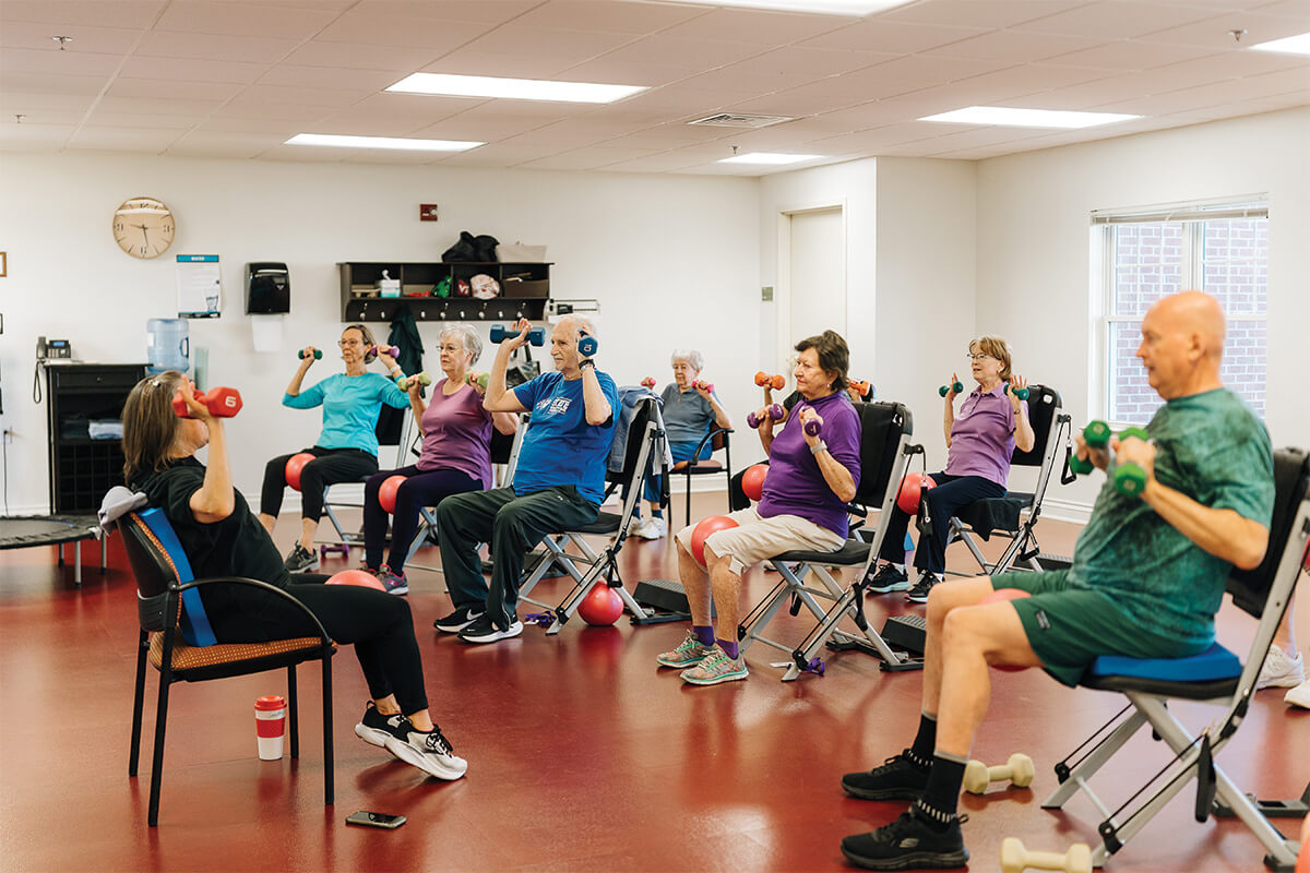 Group exercise session with seniors lifting small dumbbells in a bright room.
