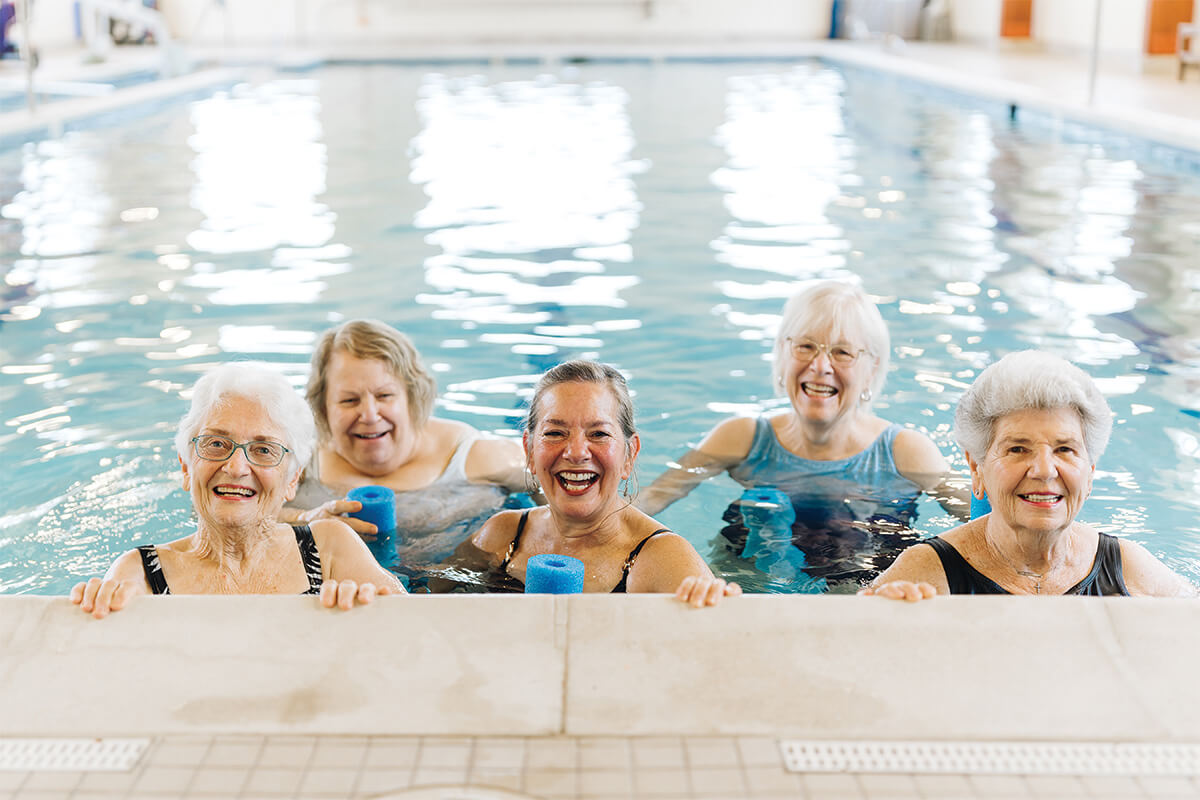Five seniors enjoy a swim in the indoor pool of a community facility.