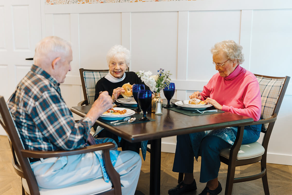 Three seniors dining together at a table in a communal dining area.